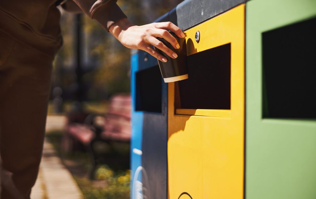 Person throwing her coffee cup into rubbish bin: simpler, standardised recycling system